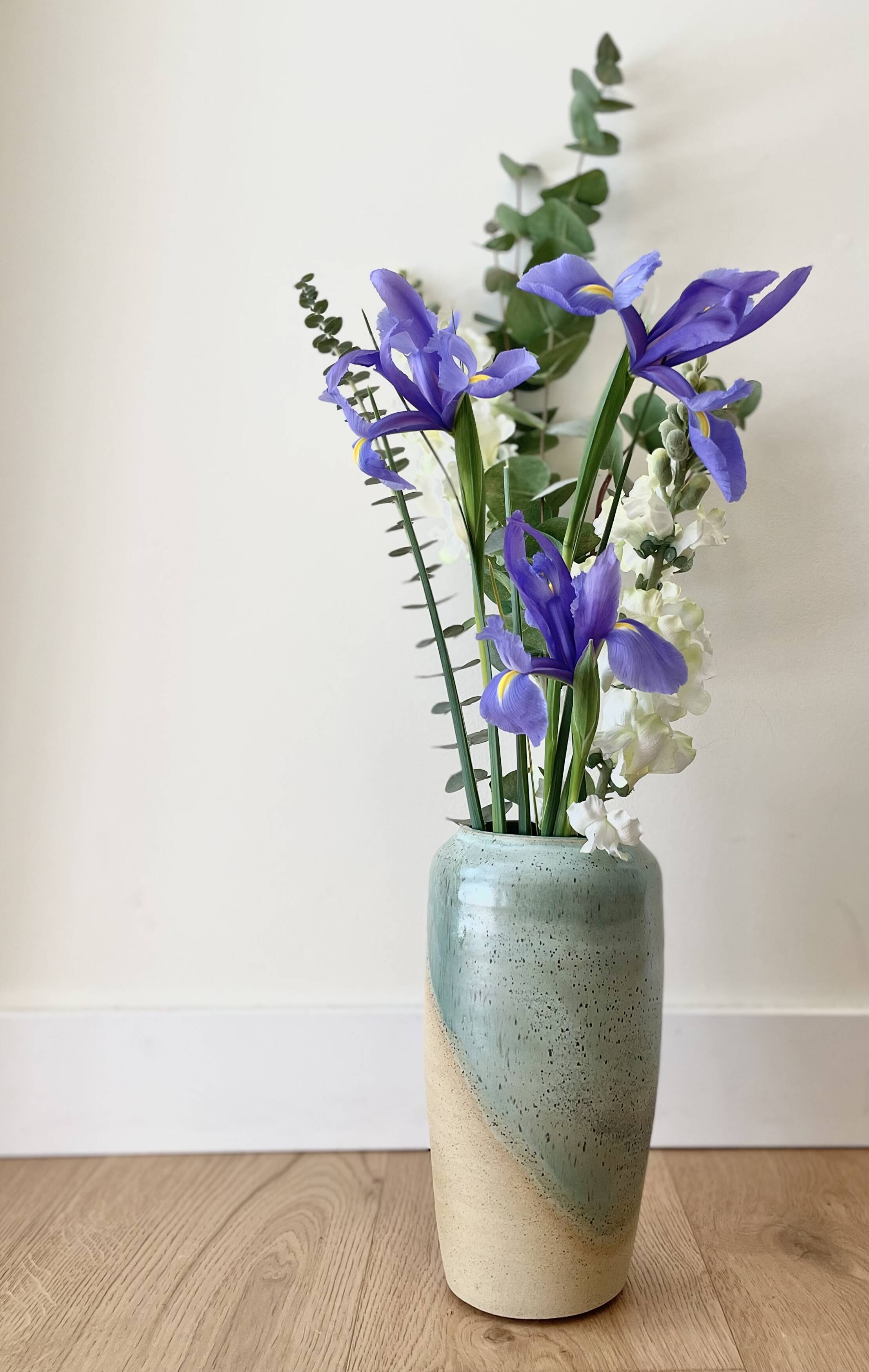 Tall handmade vase in teal and cream glaze holding purple iris flowers