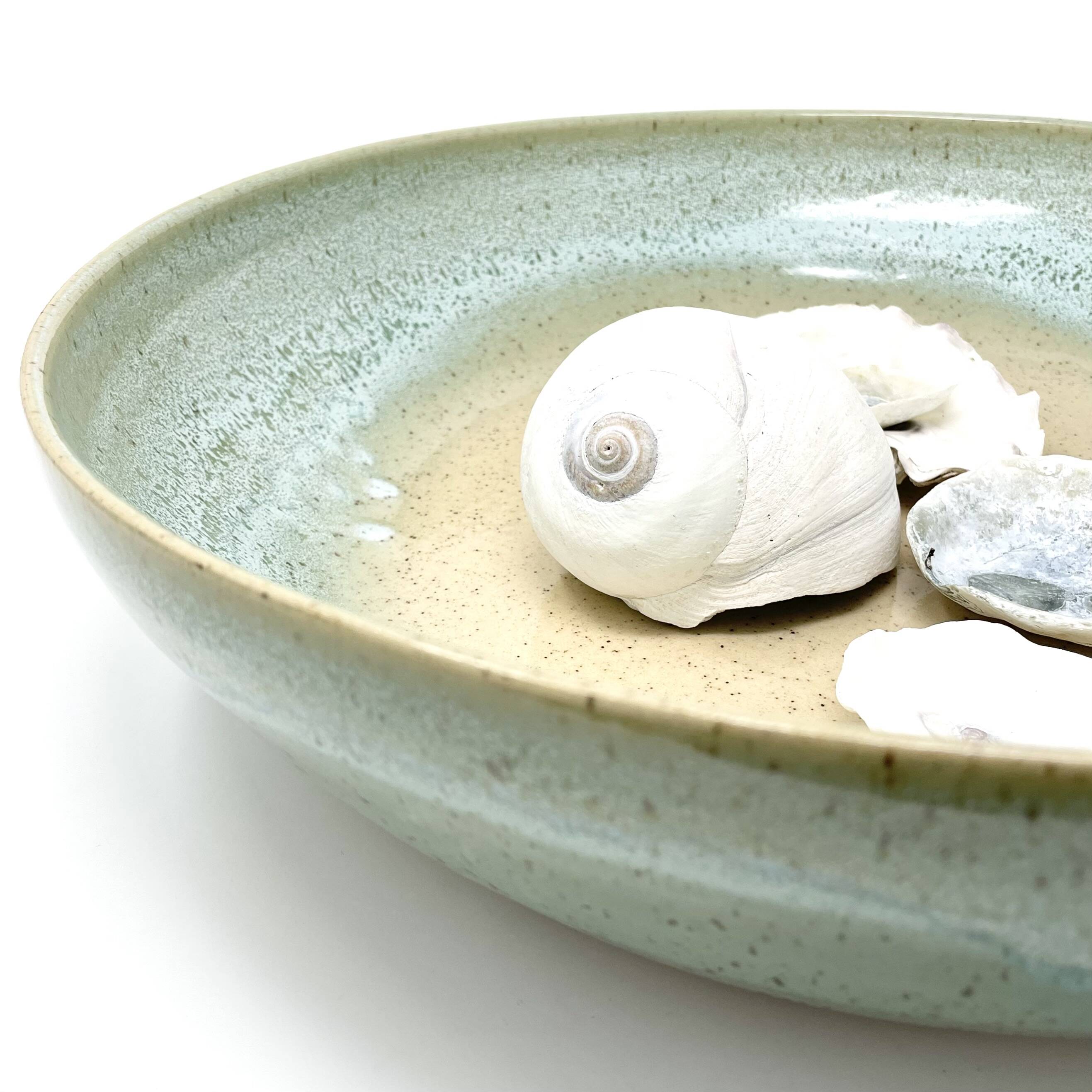 Wide shallow bowl with a pale green and sand glaze, holding seashells