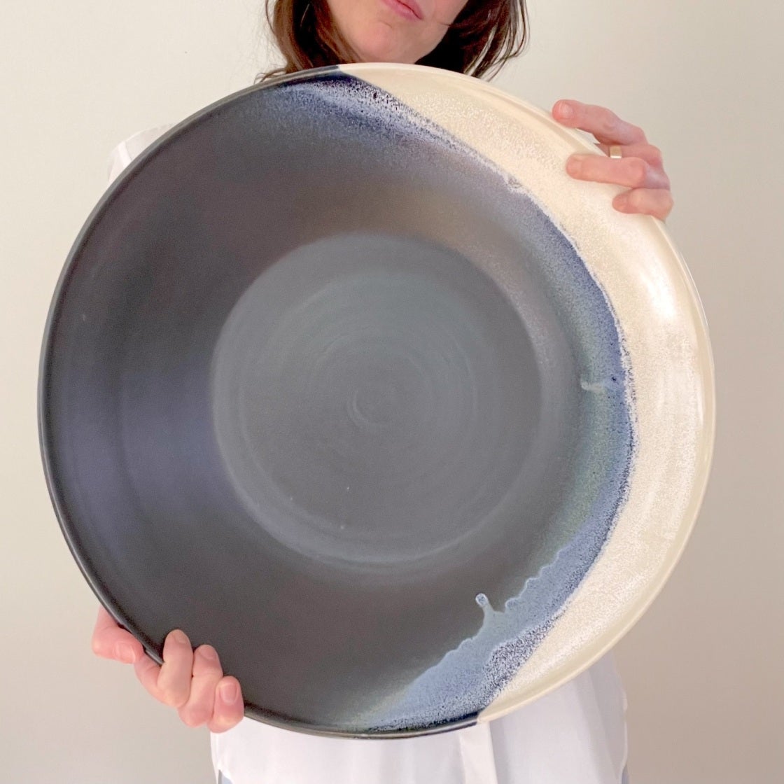 Person holding a large shallow platter glazed purple-grey with a cream rim