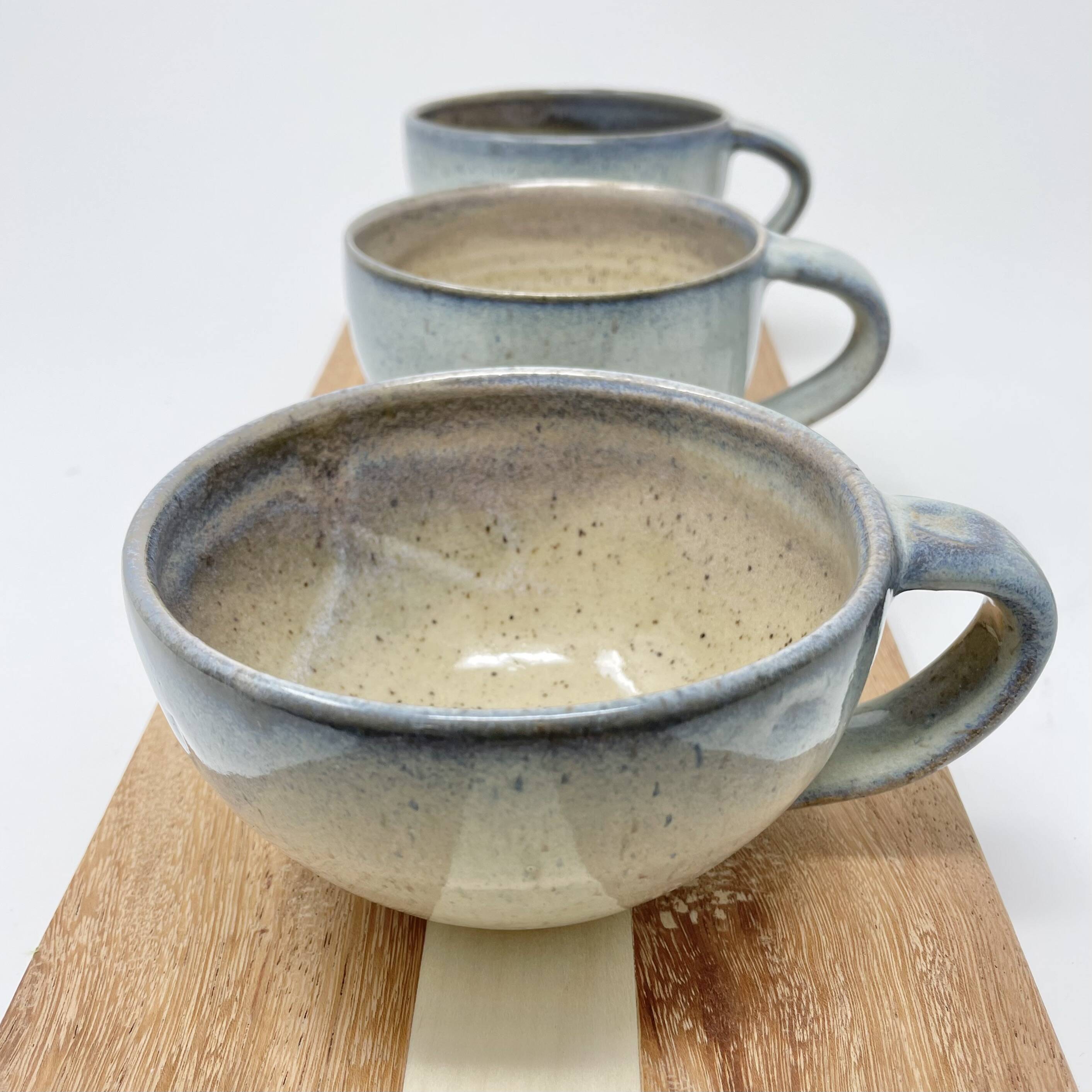 Row of wide low cups with a blue-grey speckled glaze on a wooden board