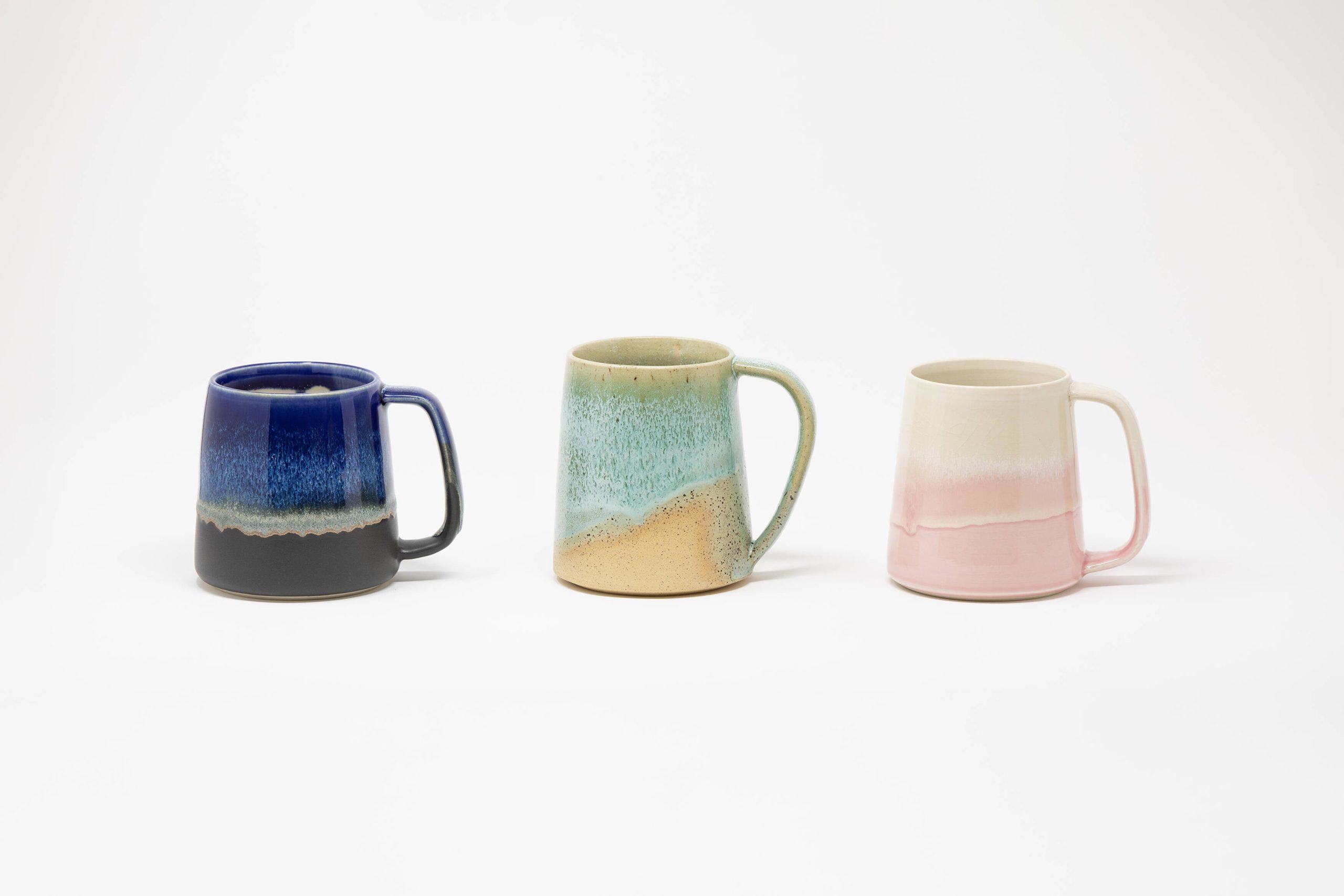 Three handmade mugs in blue, teal-and-cream, and pink glazes