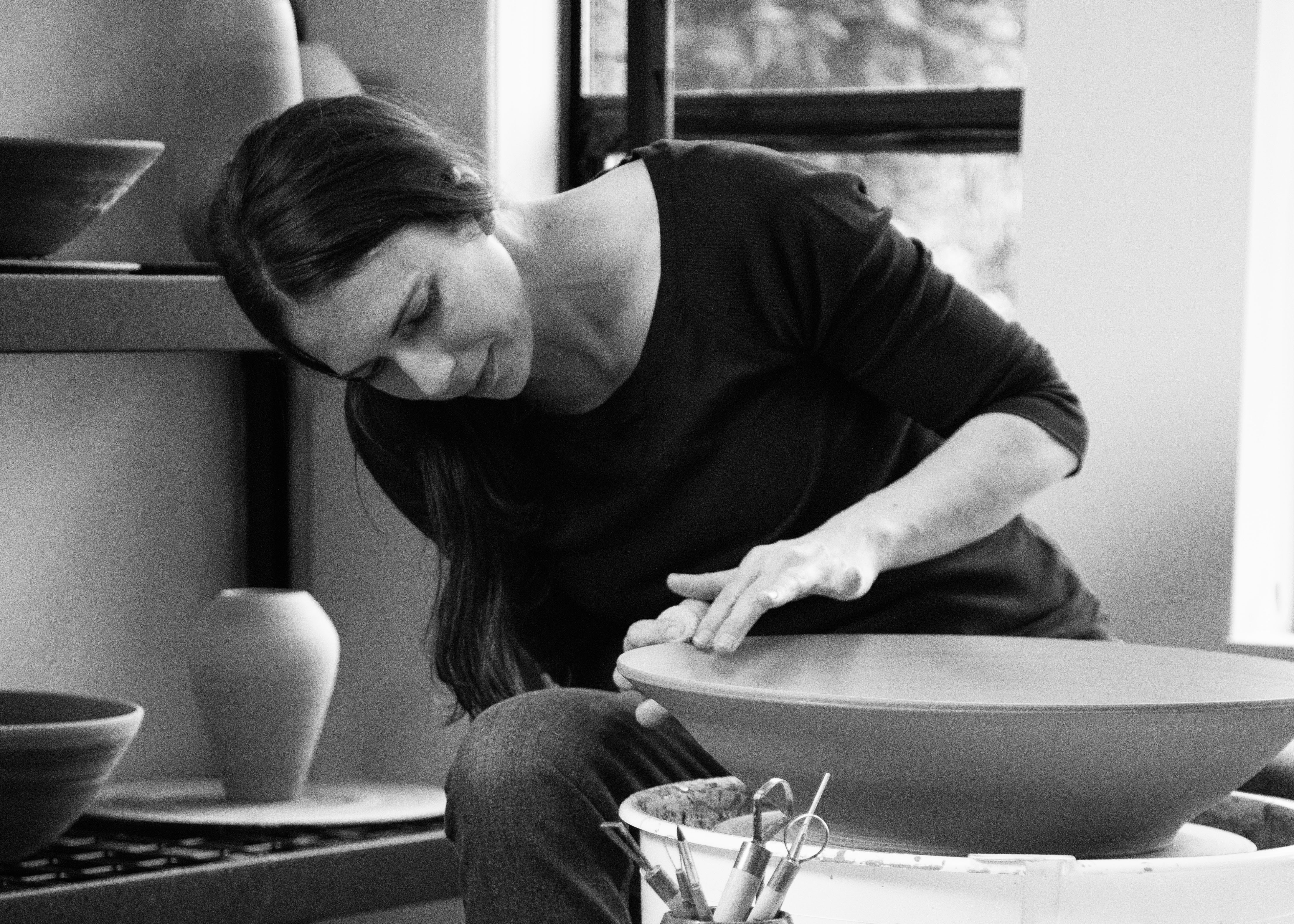 Black-and-white photo of the potter trimming a piece at her studio table