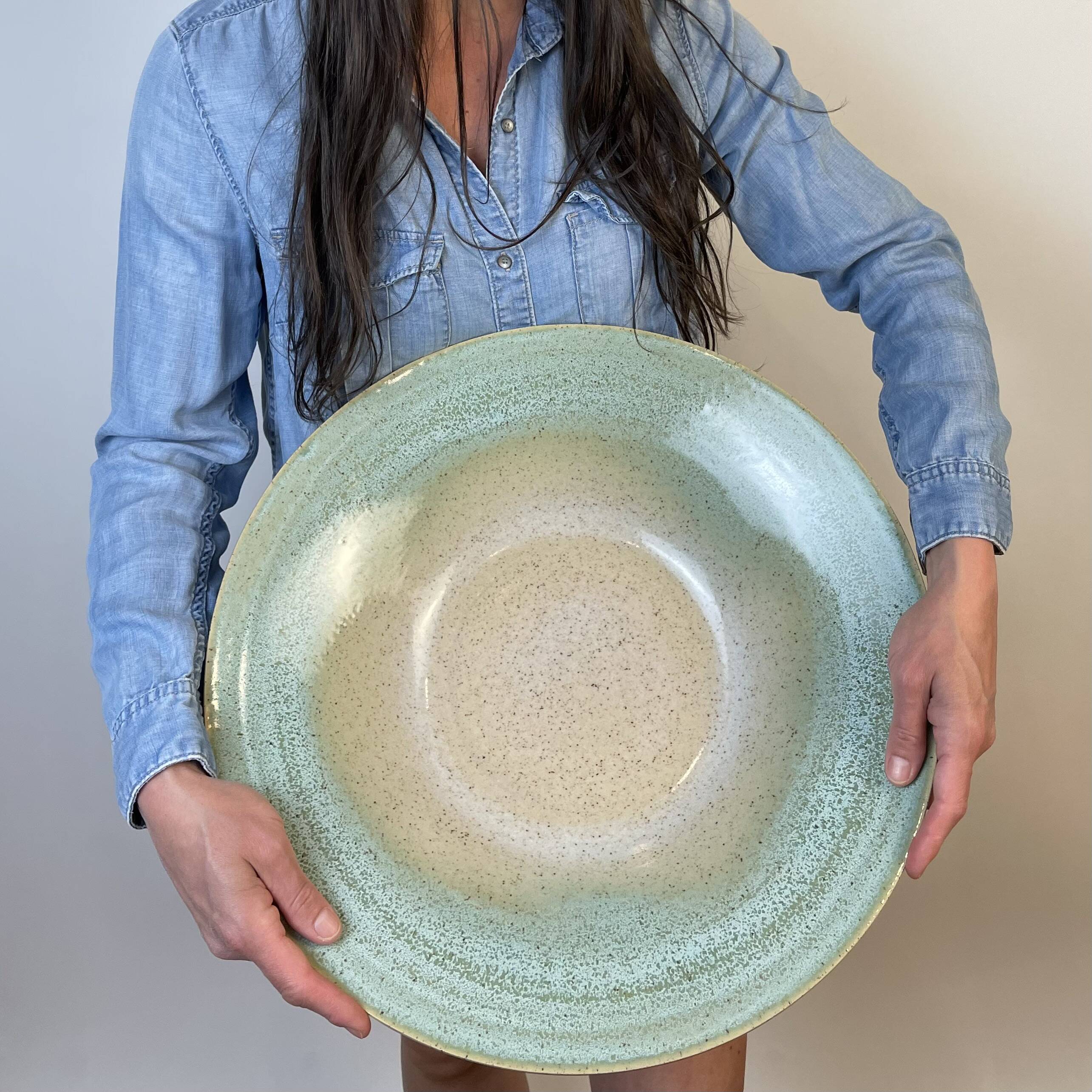 Person in a blue shirt holding a wide shallow bowl with a pale green glaze
