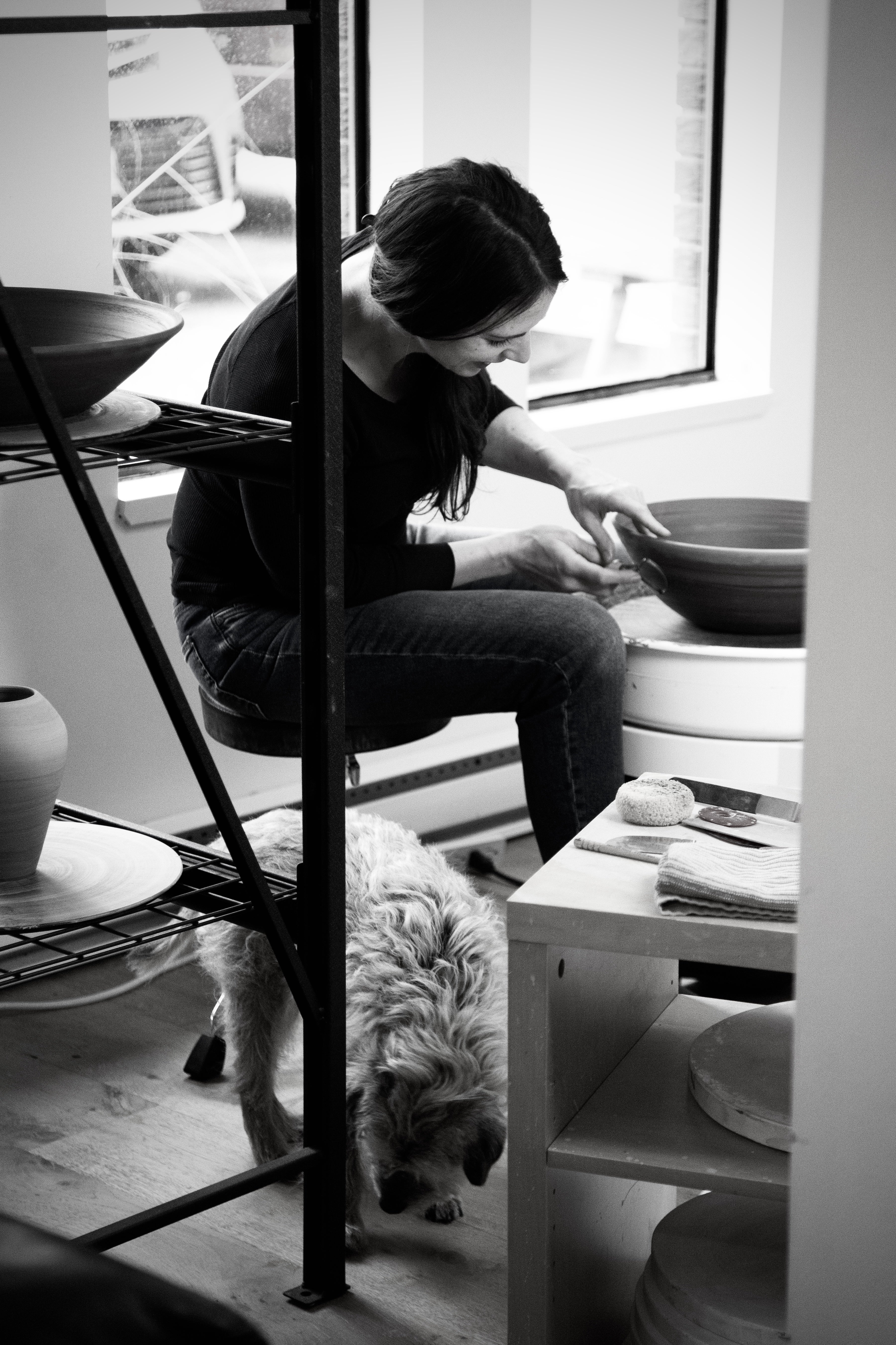 Black-and-white photo of the potter working at her wheel in the studio