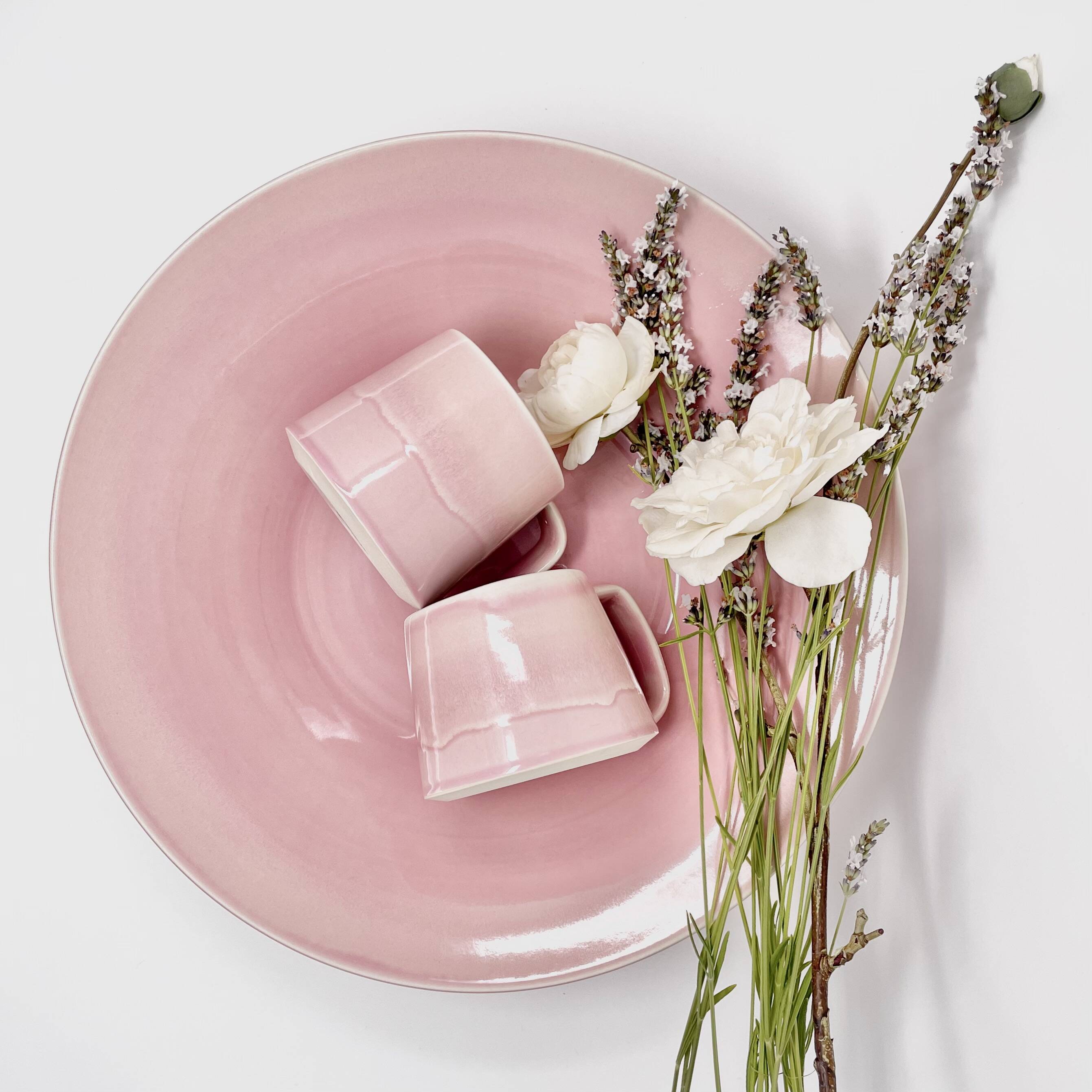Pink glazed plate with small matching cups and dried flowers