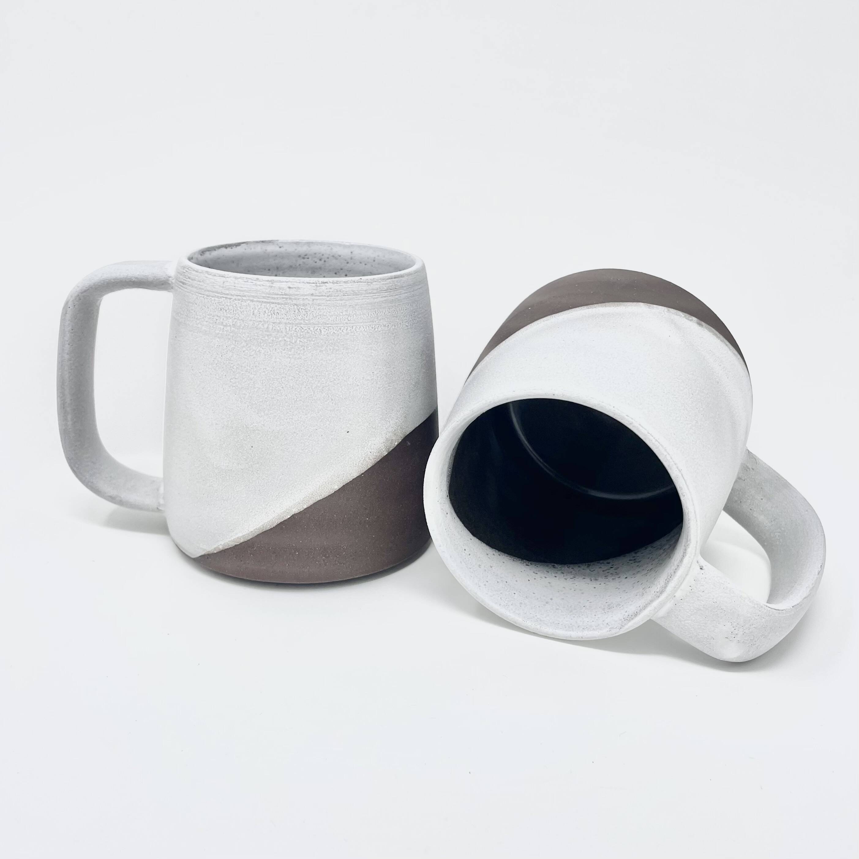 Two mugs with white glaze over dark clay, one revealing a dark blue interior