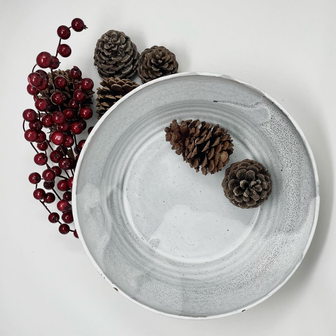 Grey speckled shallow bowl with pinecones and red berries