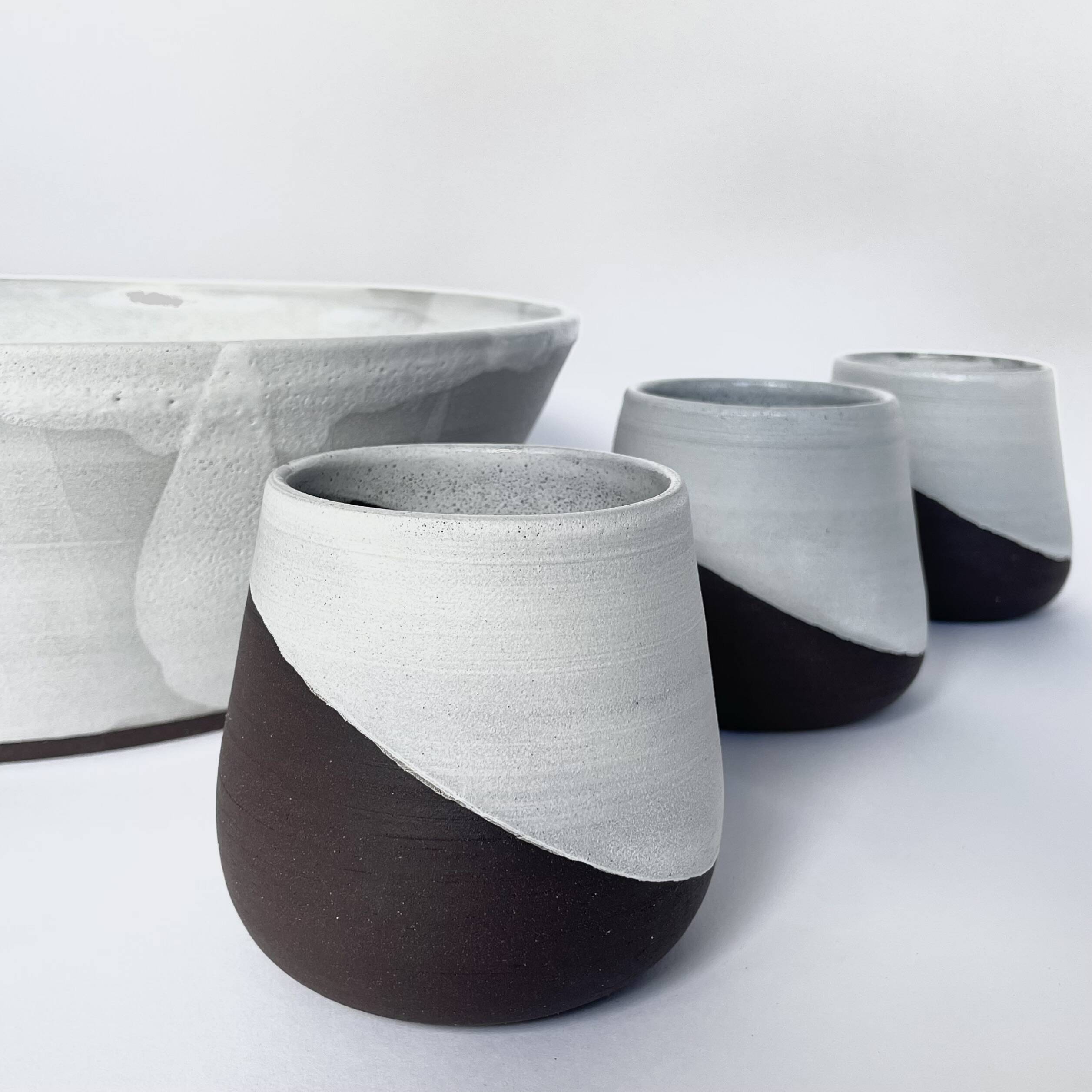 Row of tumblers with white glaze dipped over dark clay