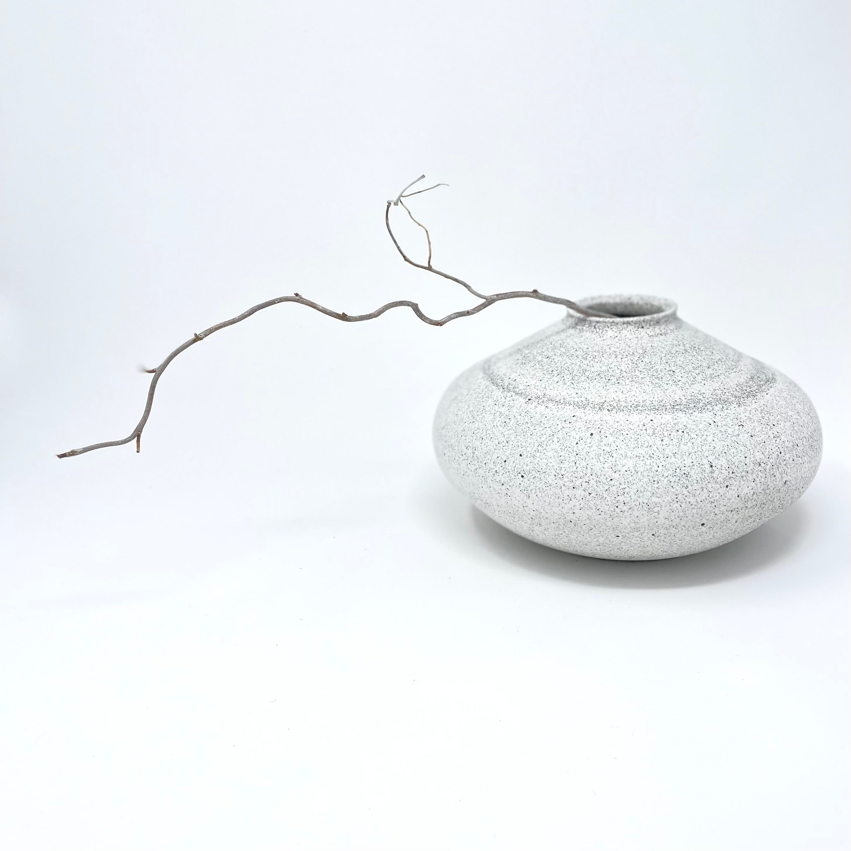 Low rounded white speckled vase with a single curling twig