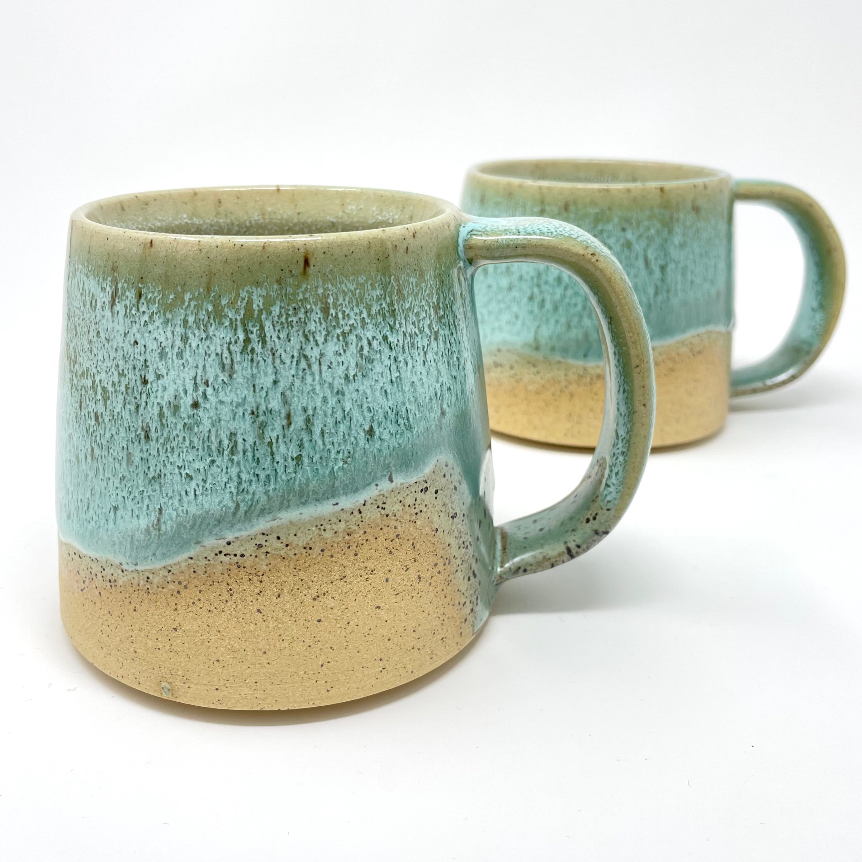 Two mugs with a seafoam-teal glaze over a sandy cream base