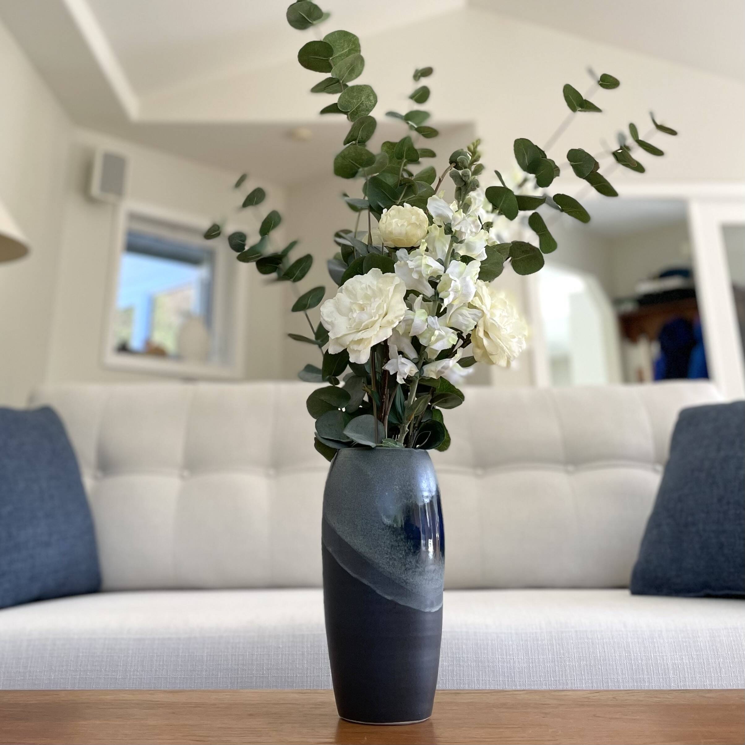 Dark blue glazed vase holding white flowers and eucalyptus in a living room