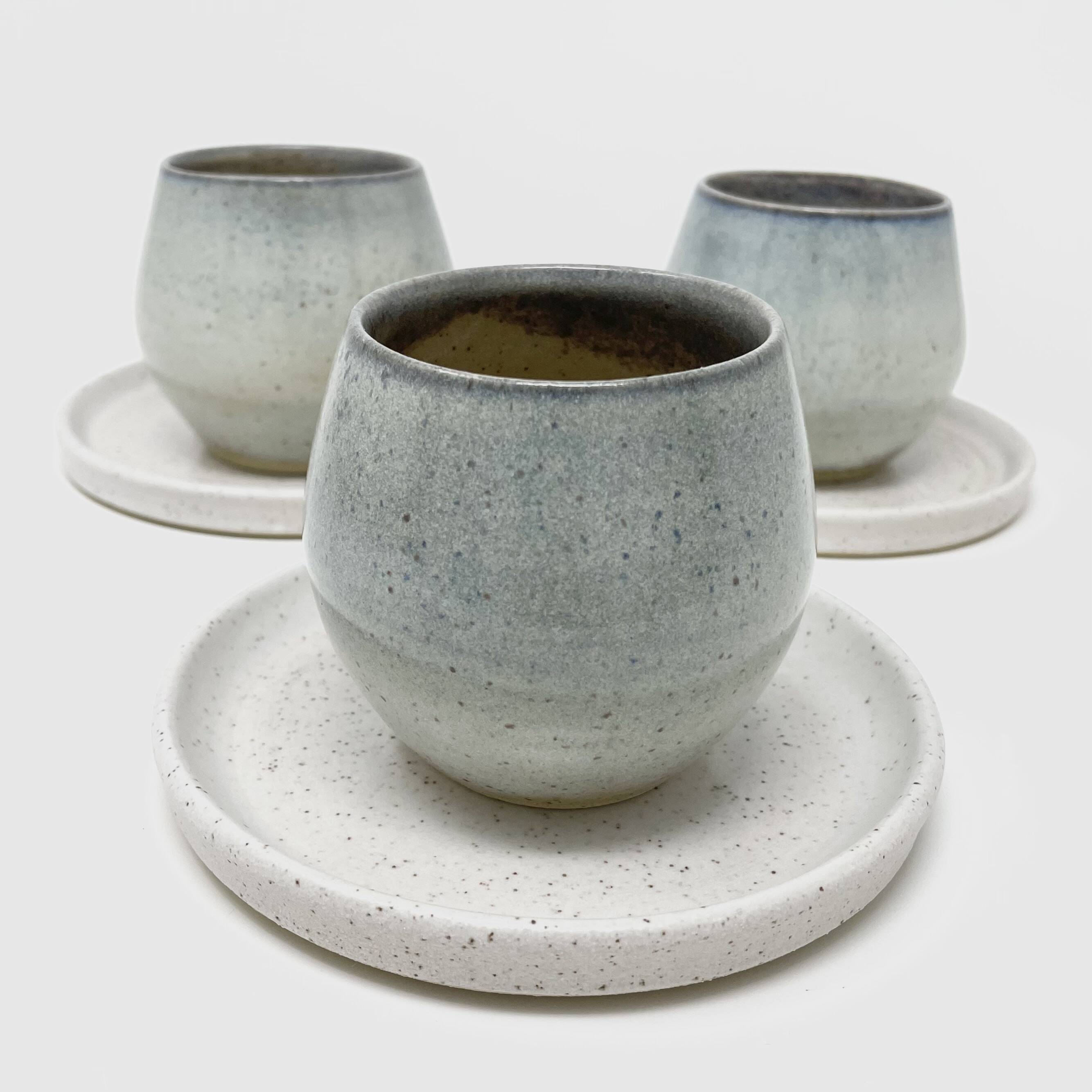 Two blue-grey glazed cups on saucers, one filled with coffee