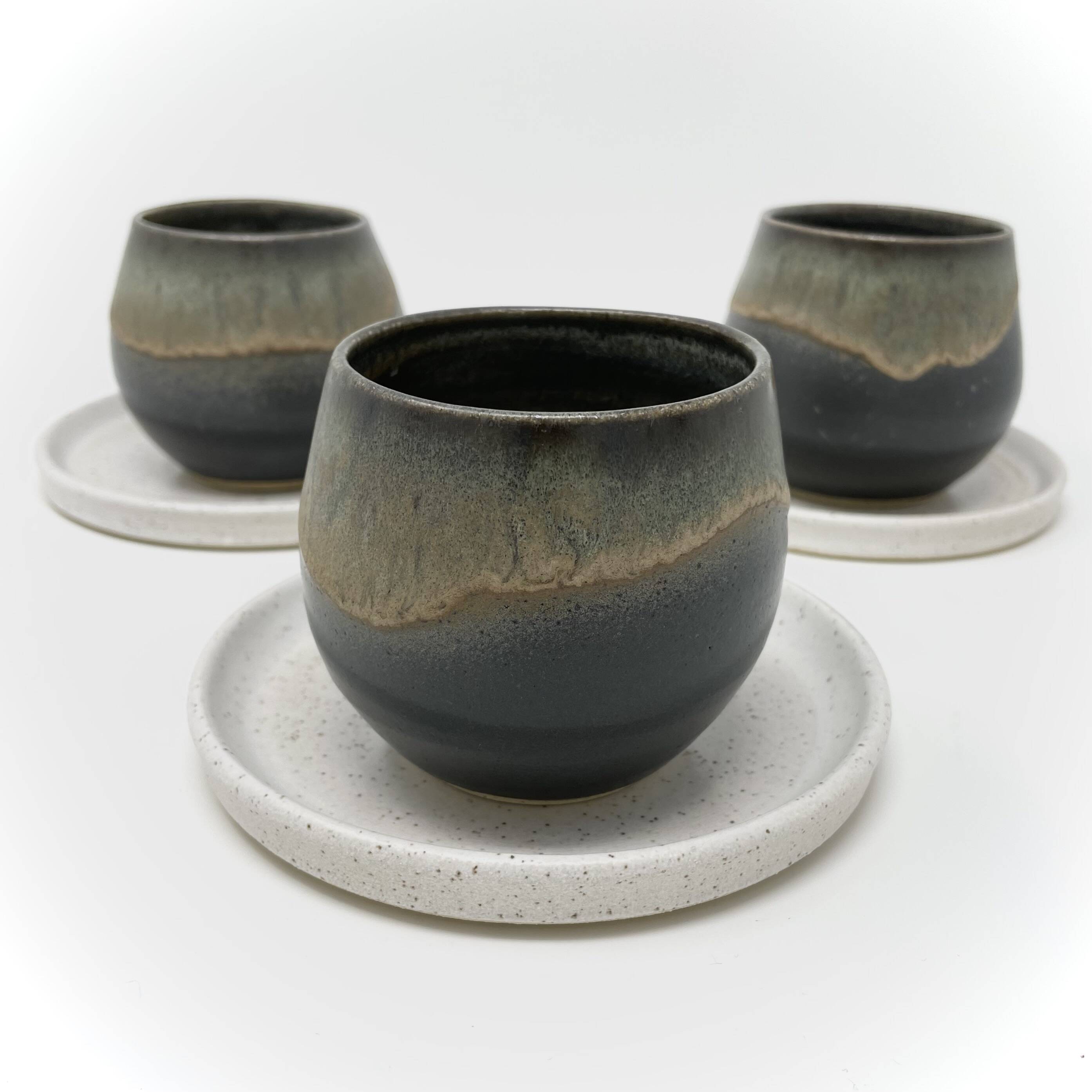 Three cups with a dark glaze and lighter drip on a saucer