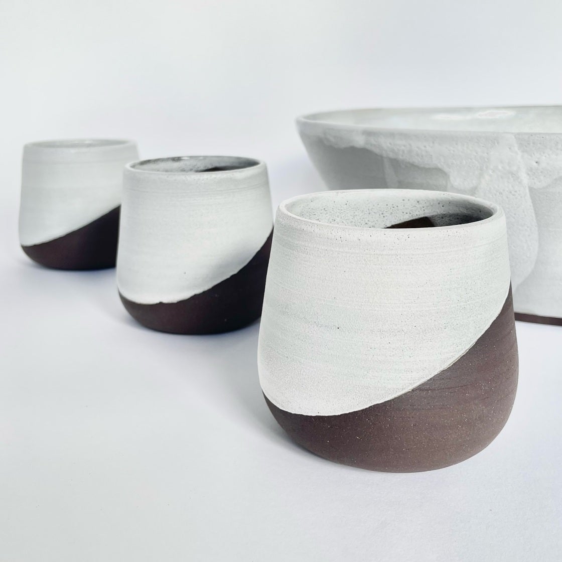 Row of tumblers with white glaze over dark clay