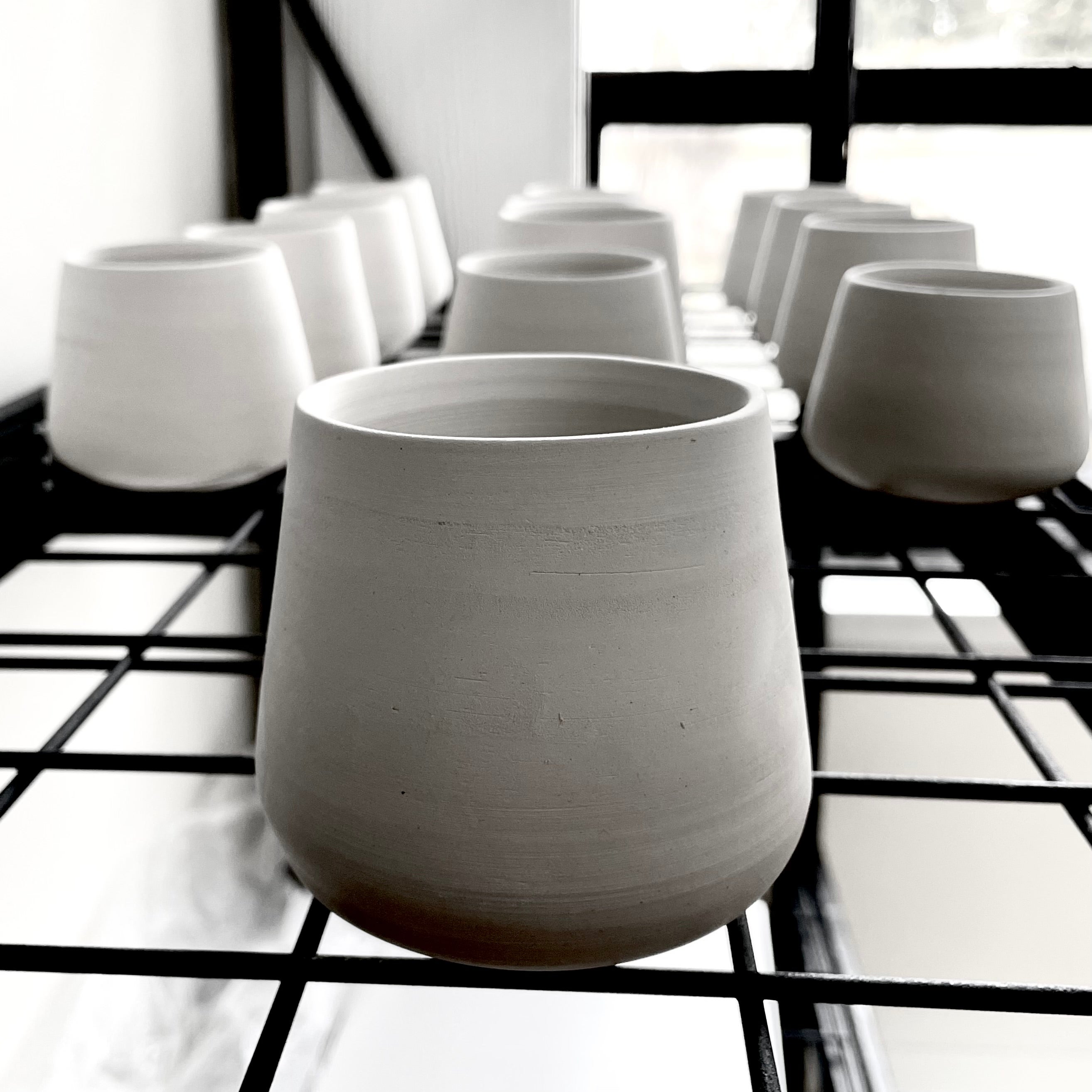 White ceramic tumblers arranged on a black grid shelf