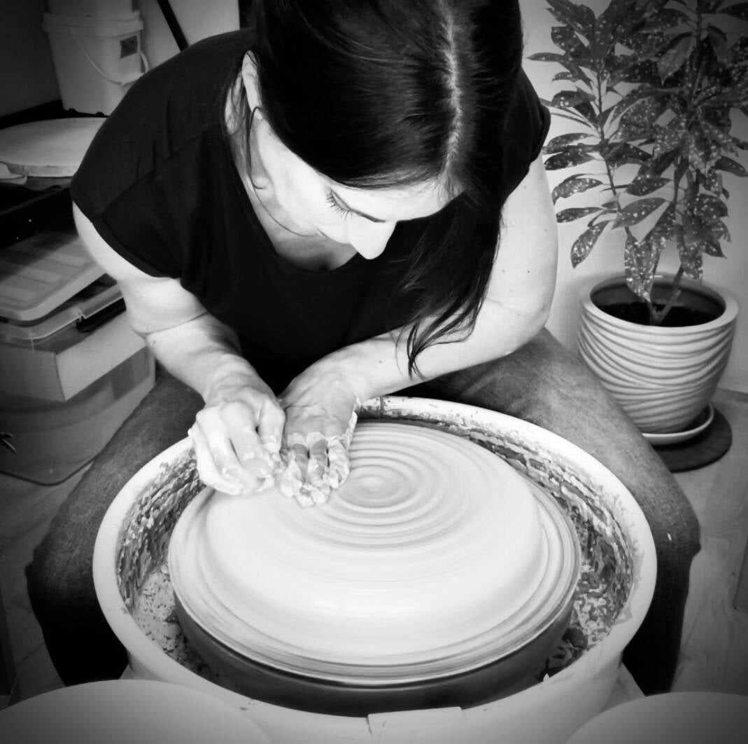 Black-and-white photo of the potter centering clay on the wheel
