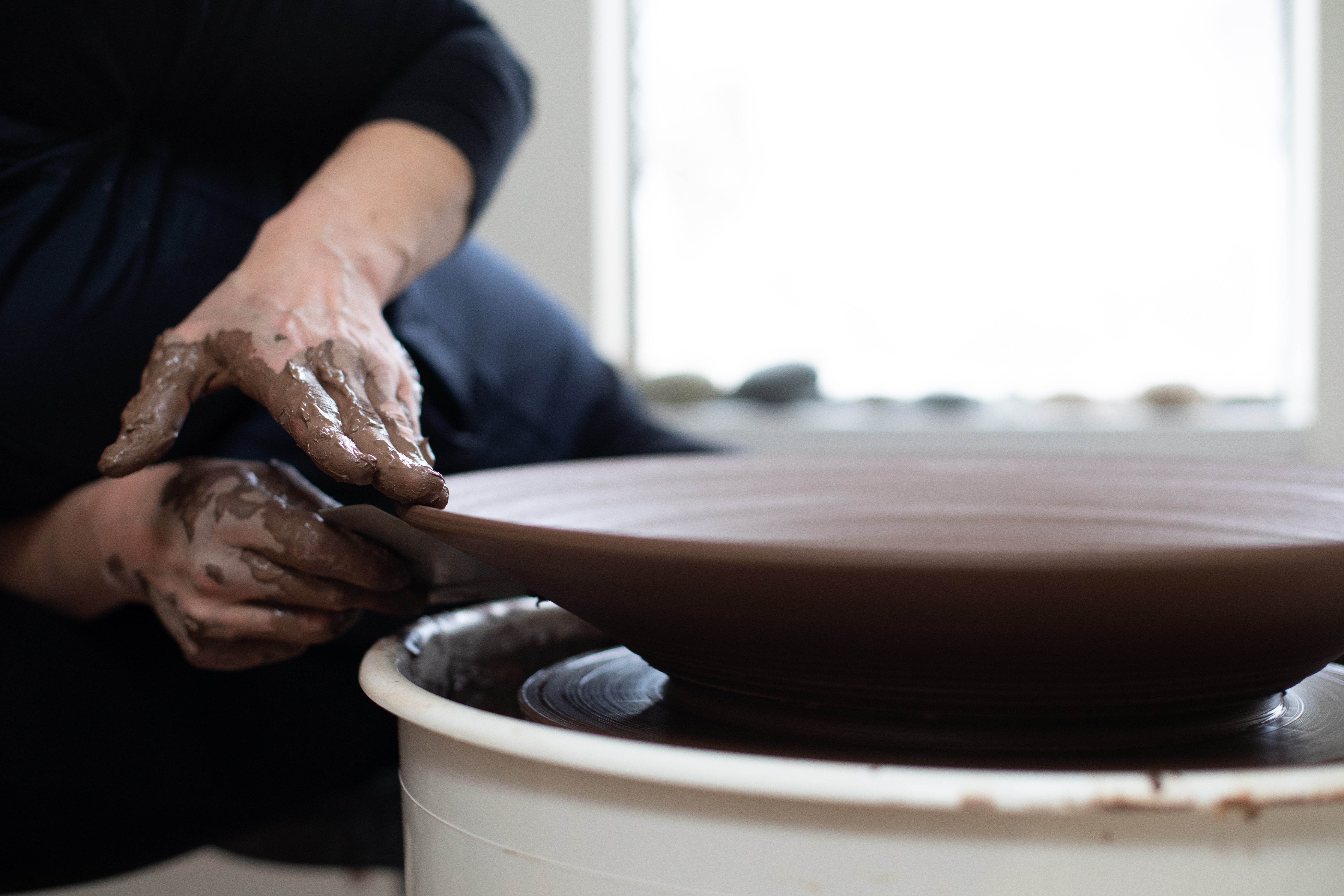 The potter's hands shaping a large bowl on the wheel