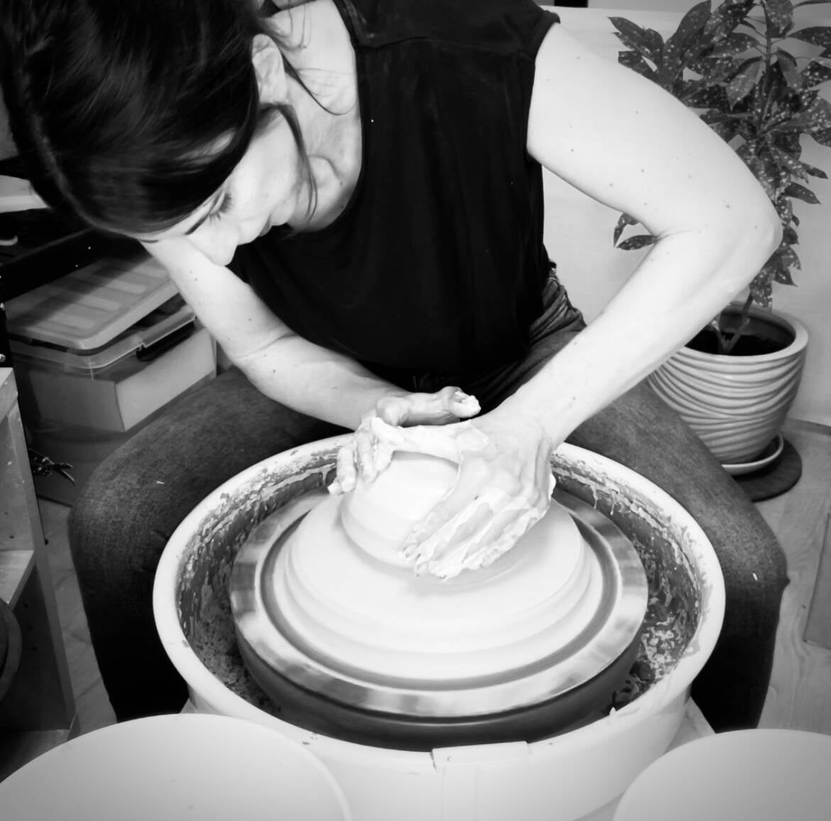 Black-and-white photo of the potter throwing a pot on the wheel