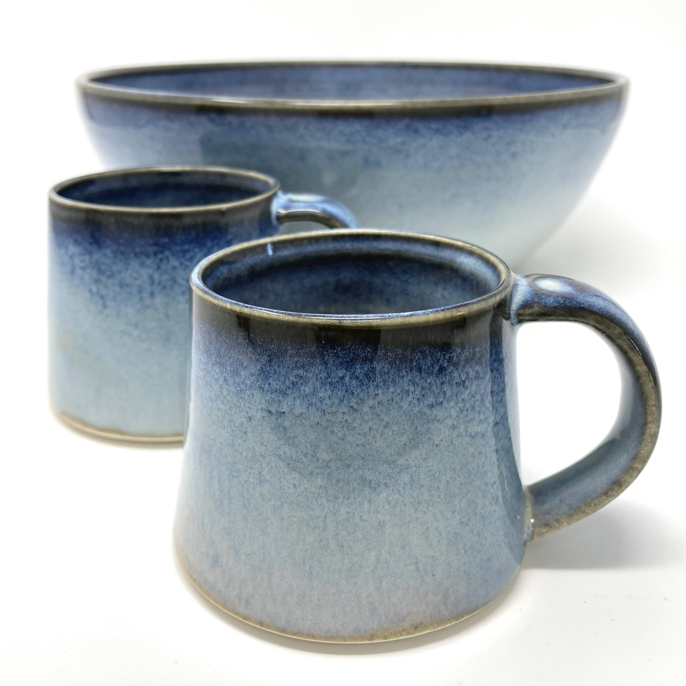 A bowl and two mugs with a blue speckled glaze fading to white