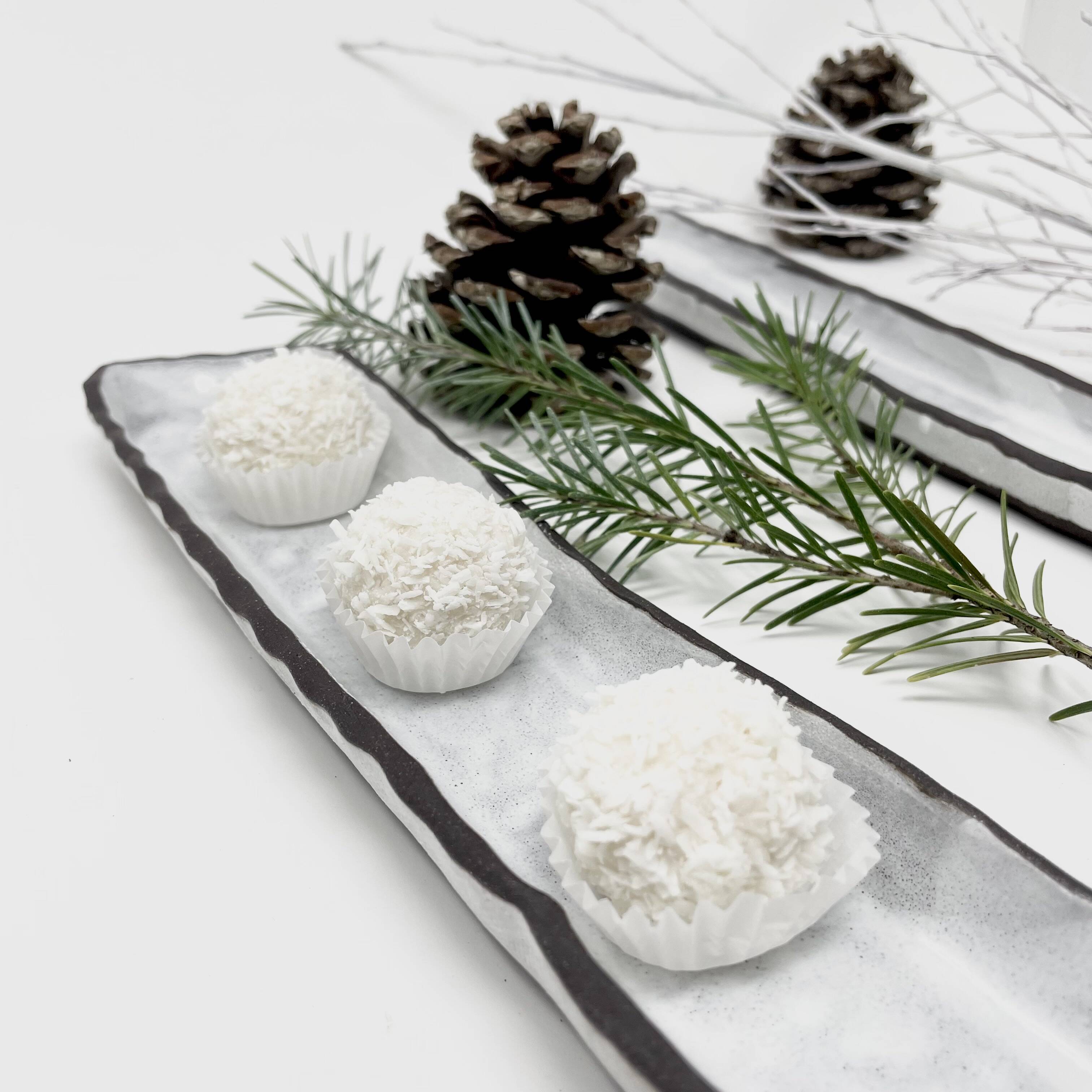 Long narrow serving tray holding pinecones, greenery and three white rounds